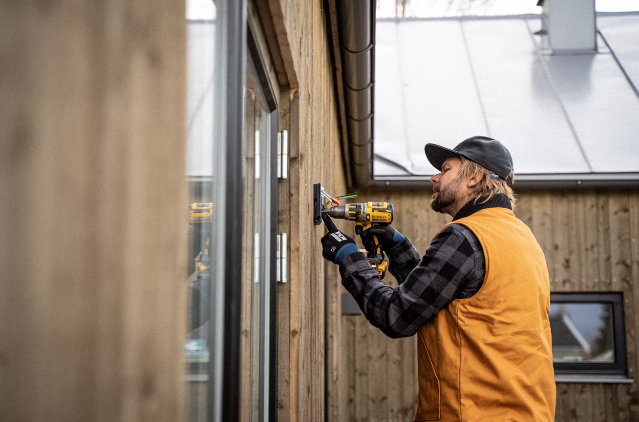 Elektriker monterar ett eluttag på fasaden till ett trähus